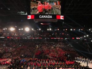 Team Canada enters the arena at the opening ceremony for the 2017 Invictus Games. The photo, which was shot from the stands above, shows a huge crowd of competitors on the lower floor level of the Air Canada Centre. Above them is jumbotron that says CANADA and shows some individual Canadian competitors. Photo: Joyce Grant, TKN