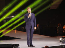 Prince Harry speaks at the opening ceremony of the 2017 Invictus Games in Toronto, Ontario. The photo shows him in a suit holding a microphone, talking. Behind him are green streaks of light (they are part of the decoration but they're pretty cool looking)