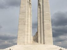 Photo of the enormous, striking and very moving Vimy War Memorial in France. There is a teenager in the foreground and the two towering spires of the monument in the background, against a light bluish-grey sky.